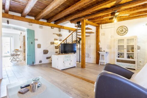 Spacious living room with exposed wooden beams and modern spiral staircase in Vrbanj stone house with pool.