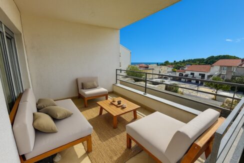 Covered balcony with lounge seating and distant sea view from a Hvar apartment.