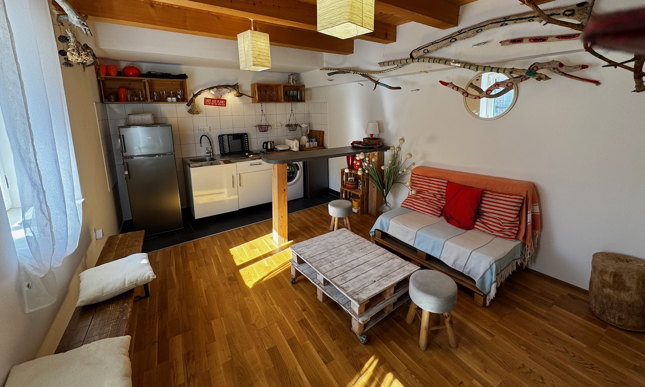 Open-plan living and kitchen area with wooden beams, sofa seating, breakfast bar and timber flooring.