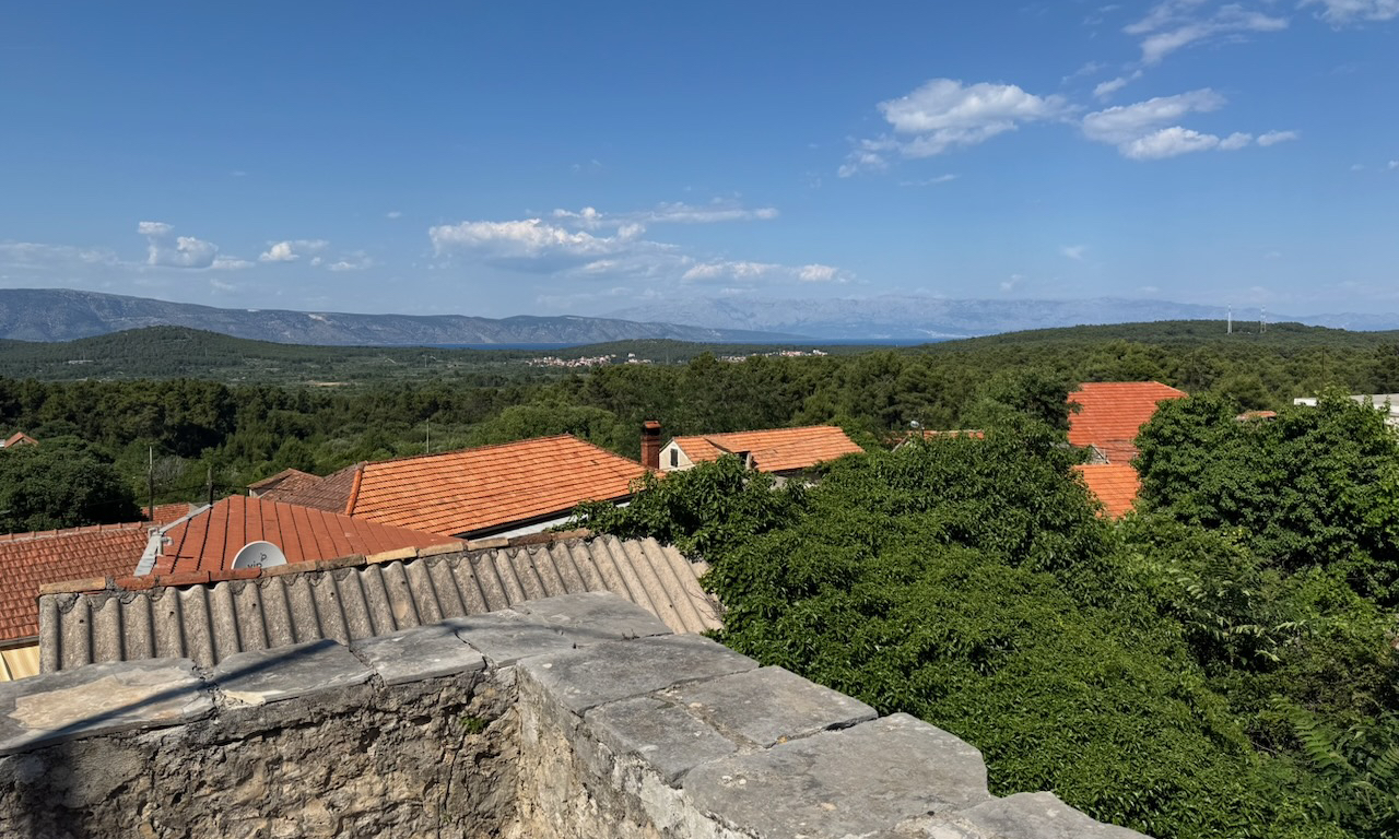 Terrace view over red rooftops, green woodland, distant sea and mainland mountains from the Vrbanj stone house.
